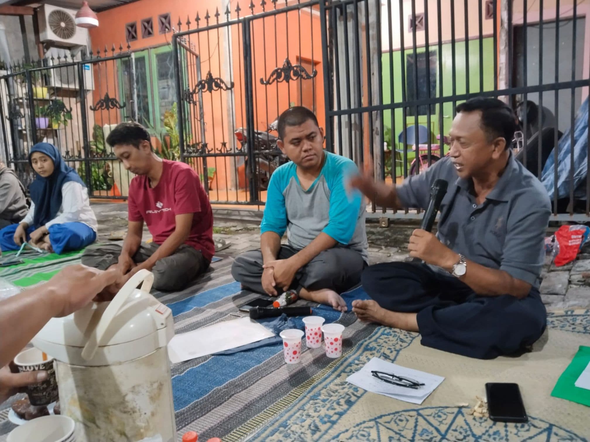 Ketua RT memegang mikrofon menjelaskan gagasan UMKM 34 dalam temu warga lesehan